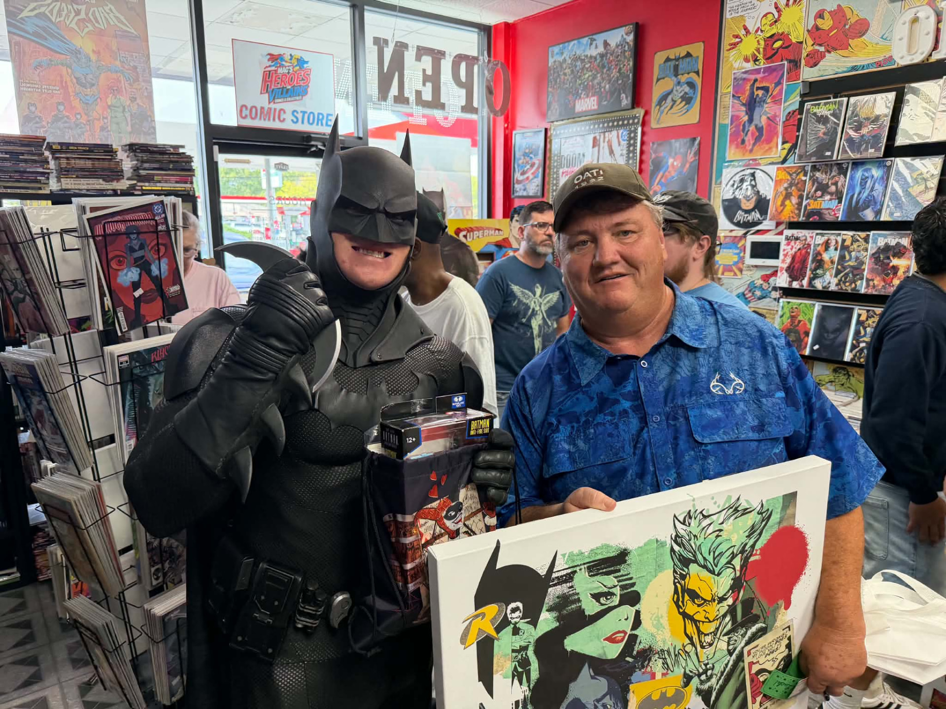 Batman greeting a fan holding a comic-art canvas inside the shop