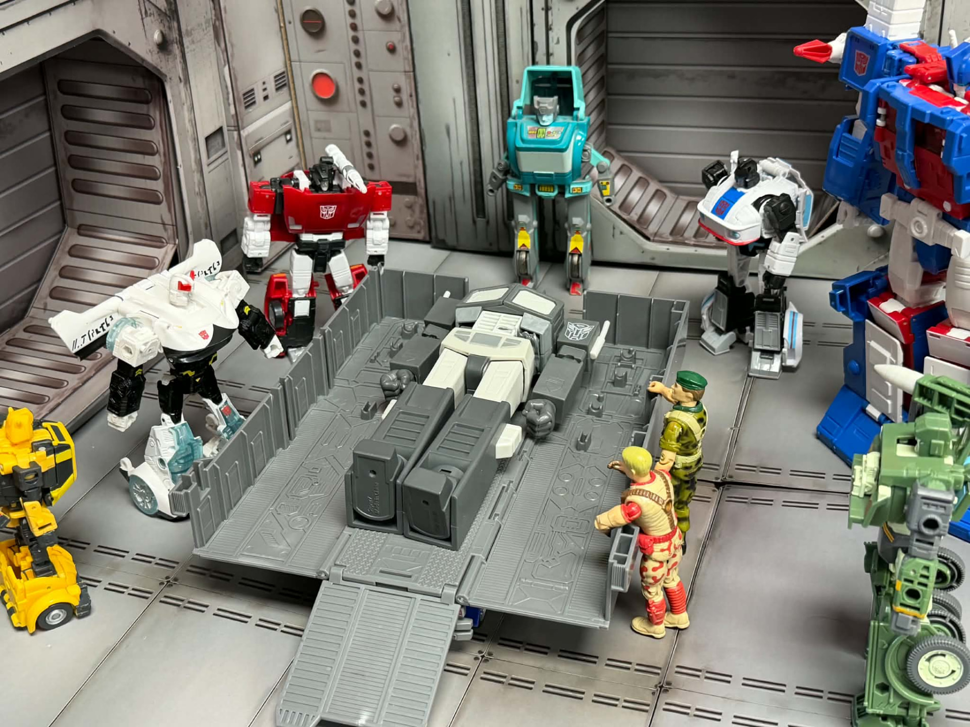 Robot figures gathered around a repair bay with two soldiers looking on
