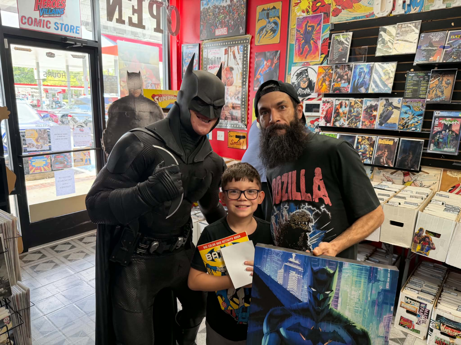 Batman with a father and son holding a Batman coloring book and canvas art