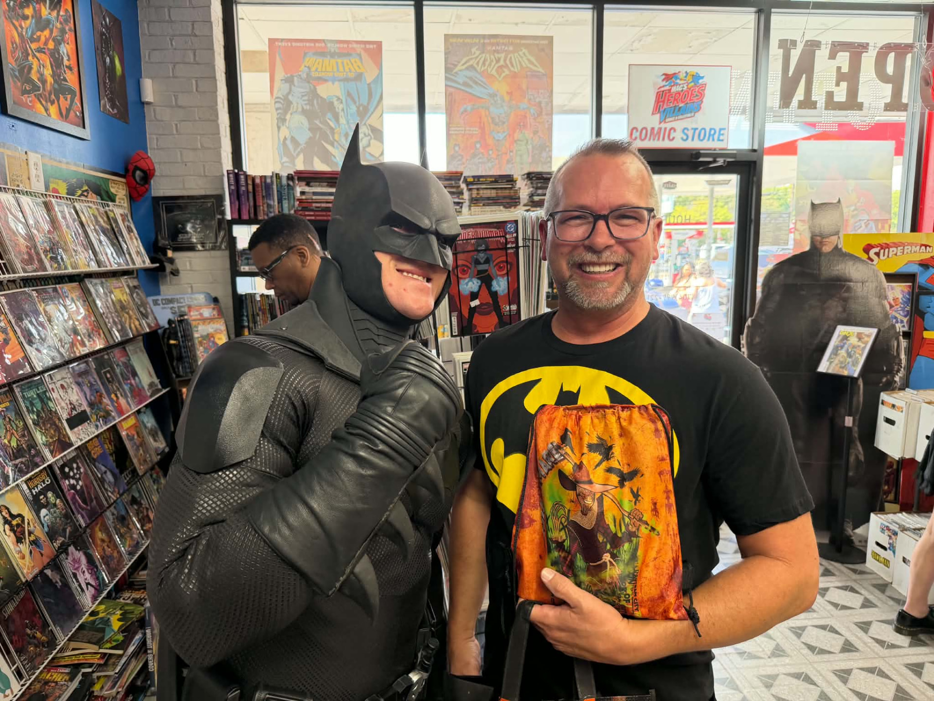 Batman posing with a fan wearing a Batman shirt at the shop door