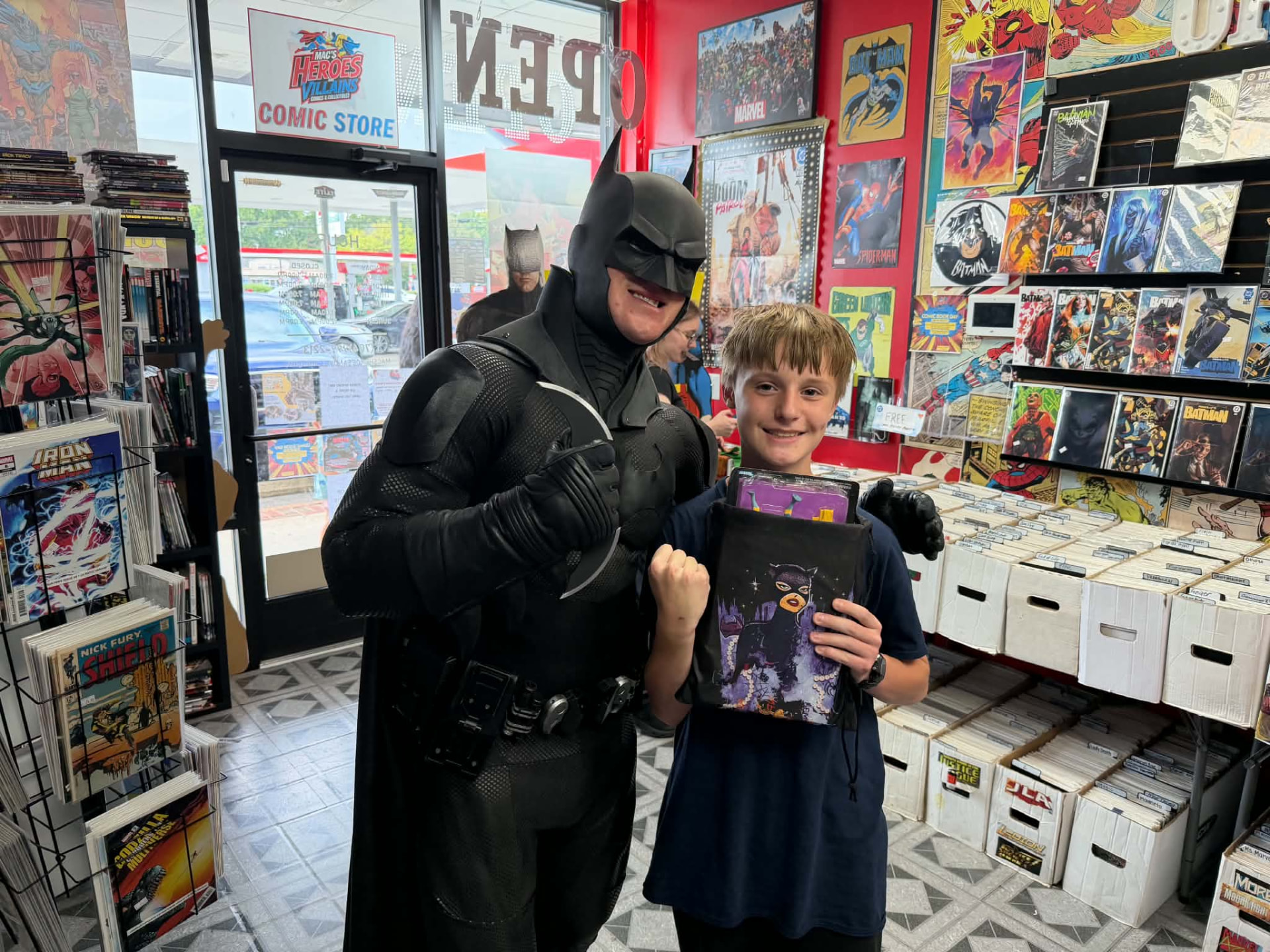 Batman posing with a young fan flexing while holding a Catwoman drawstring bag