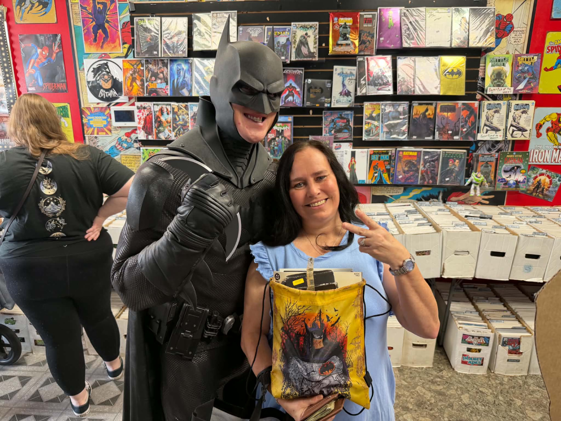Batman posing with a customer carrying a Batman drawstring bag full of comics